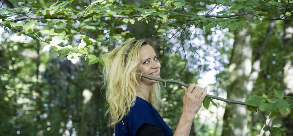 Utøver med et blad i hånden, omgitt av grønt løvverk.