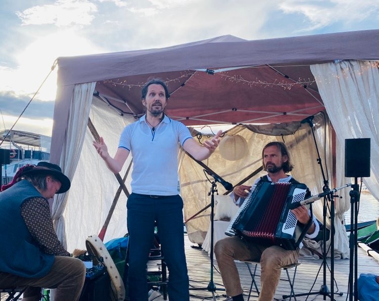 Tre musikere spiller under en hvit teltduk, med trekkspill og tromme.